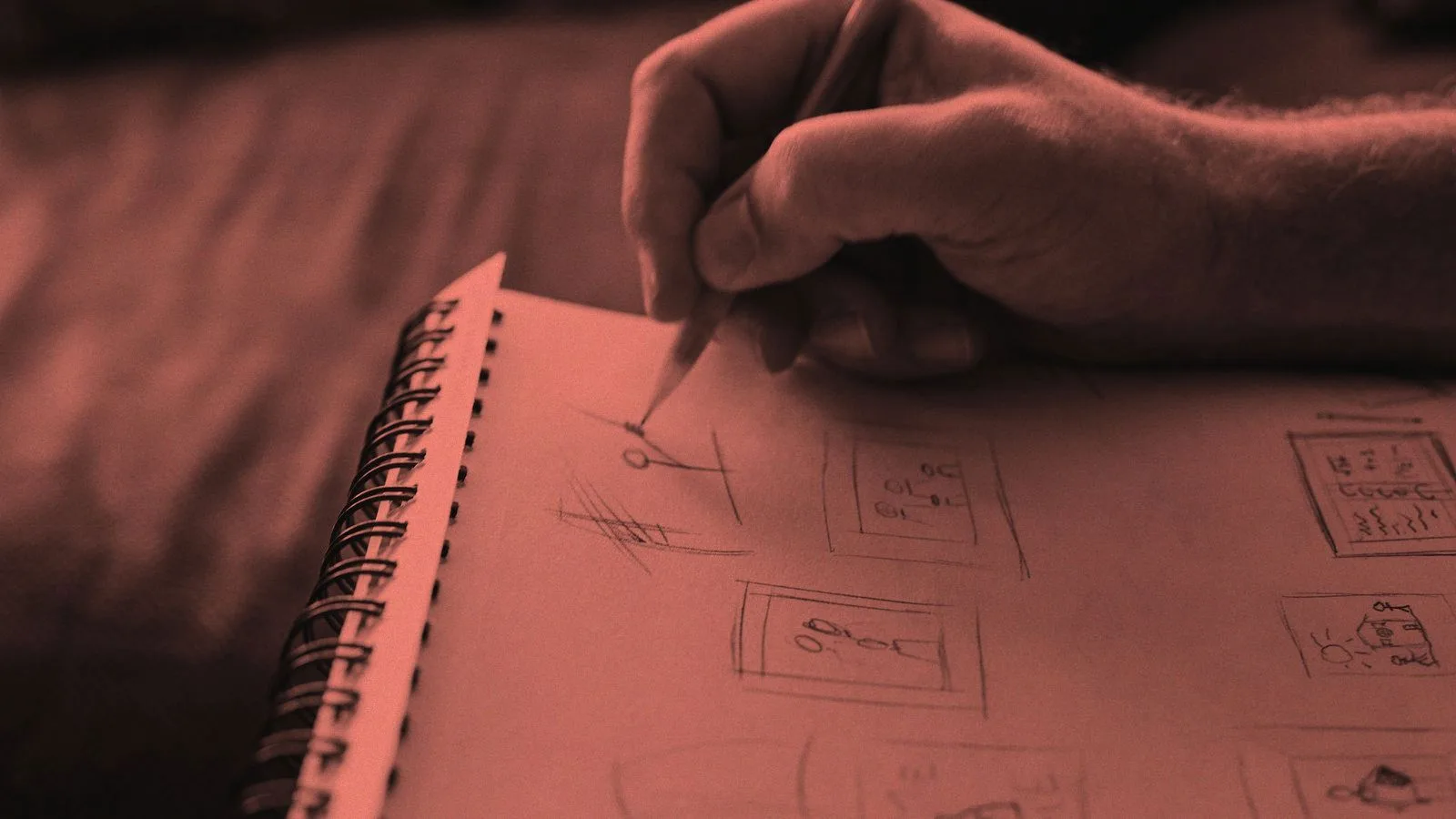 A hand sketching storyboard frames in a spiral notebook